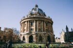 This image shows the iconic Radcliffe camera in the Oxford city centre, a large, grand, circular building made of pale stone with a grey domed roof.