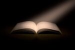 An open book illuminated by a beam of light.