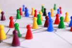 Red, purple, green, yellow, blue and black playing pieces representing people are spread across a white surface. Some of the pieces are connected by grey lines drawn on the surface, representing connections between people.