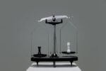 A black and white scale with unevenly weighted chess pieces. The black rook on the left platform of the scale is heavier than the white rook on the right.