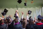 Students wearing black graduation gowns throw graduation hats in the air