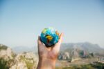 Hand holds small model of the globe infront of a mountain landscape